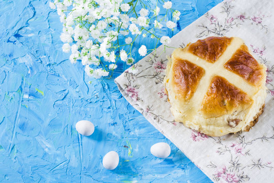 Traditional Easter hot cross buns with chocolate eggs on napkin and sky blue background. Traditional bakery with flowers.