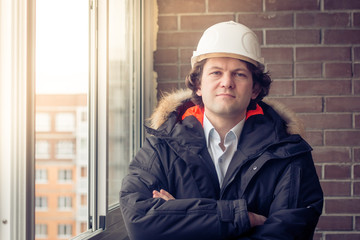 Portrait of engineer wear white safety helmet and cross his arms on construction site with brick background. Soft focus, toned.