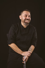 Portrait of a smiling chef looking to the rigth holding a knife on a black background.