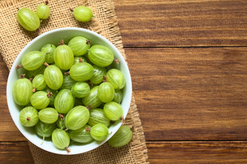 Raw gooseberries (lat. Ribes uva-crispa) in bowl, photographed overhead on dark wood with natural light (Selective Focus, Focus on the gooseberries on the top)