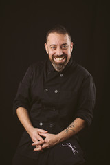 Portrait of a smiling chef looking at the camera on a black background.