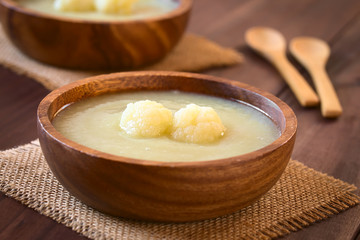 Cream of cauliflower soup in wooden bowl, photographed on wood with natural light (Selective Focus, Focus on the cauliflower on the soup)