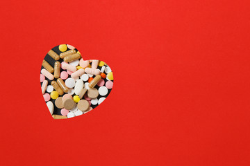 Medication white colorful round tablets arranged abstract in heart shape on red color background. Pills for design. Health, treatment, choice healthy lifestyle concept. Copy space for advertisement.