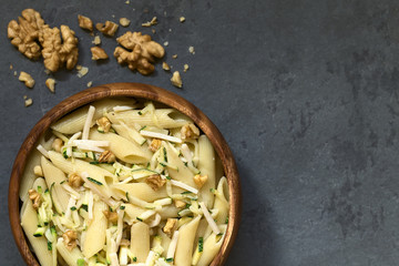 Penne pasta with zucchini and ham stripes and walnut served in bowl, photographed overhead on slate with natural light (Selective Focus, Focus on the top of the dish)