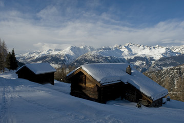 wooden mountain hut (cabin), covered by snow, ray of sunshine, on horizon snow covered mountains and ski slopes of Belalp, sunset, forest, isolated, fairytale, winter, Alps, Valais, Rothwald, Swiss