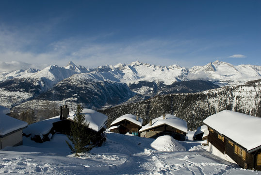 village of wooden mountain hut (cabin), covered by snow, sunshine, on horizon snow covered mountains and ski slopes of Belalp, sunset, forest, fairytale, holiday, winter, Alps, Valais, Wasenalp, Swiss