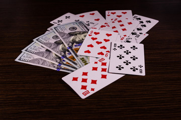 Playing cards and one hundred dollar bills on a dark wooden table