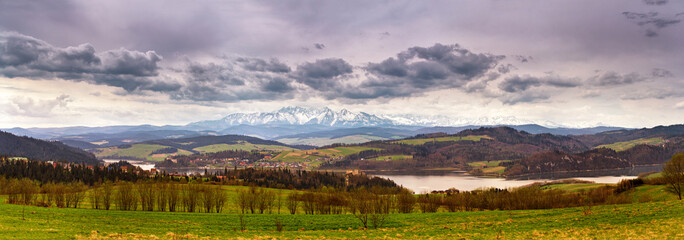 Panorama of spring snowy Tatra mountains. Lake and village behind high mountain range