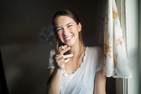 Portrait of a smiling woman smoking a joint while standing indoors