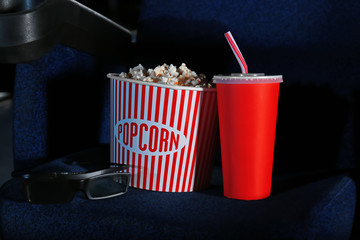 Bucket with tasty popcorn and cola on chair in cinema