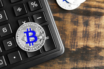 Silver bitcoin with calculator on wooden background