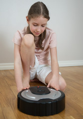 Little girl and robotic vacuum cleaner on the floor.