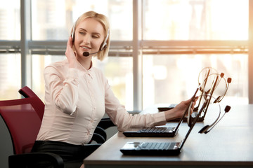 Sitting female call center operator looking back. Gaze of adorable adult female operator. Bright windows background.