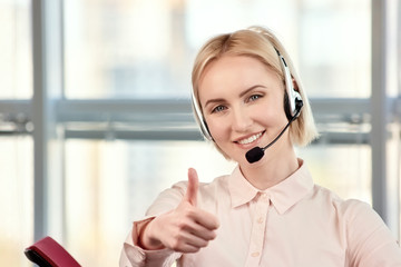 Female blond mature call center operator showing thumbs up. Smiling call center agent giving thumb...