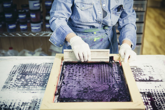 Midsection of craftswoman using silk screen to print design on fabric at workshop