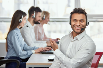 Call center operator pointing at his colleagues. Indian handsome young man pointing at his coworkers. They are working.