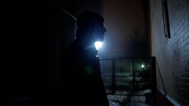 4k Black silhouette brutal man standing at gateway in lamp light winter cold night city
