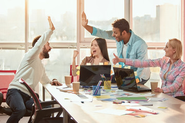 Casual colleagues doing high-five in the office. Students rejoice at the performance of work.