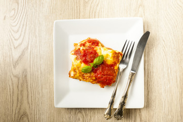 appetizing portion of lasagna on a white plate with tomato sauce