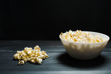 Salty popcorn lies in a white plate. The concept of cinema, watch TV shows. Junk food.