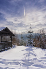 Wooden bower near mountain trail. Winter sunny day and hazy mountain in the background.