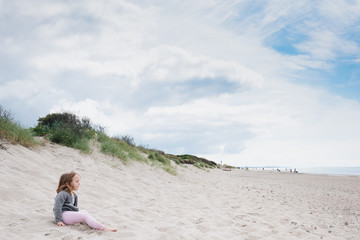 little girl sitting on a beach watching the sea