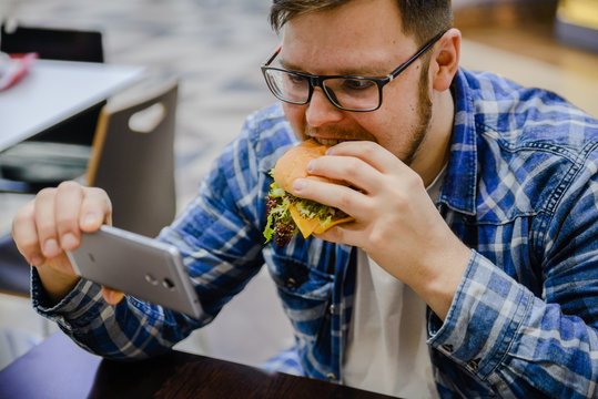 man eat hamburger while watch video on his phone
