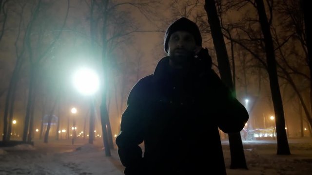 4k Middle age man talking by mobile with his friend in cold winter night city park