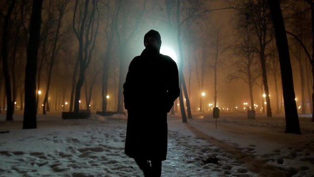 4k Black silhouette of man walks at dark winter night park with backlight wide shot