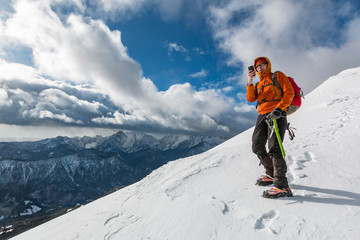 Mountaineer photographing on the snowy slope of the Dovska Baba mountain in Karavanke range,...