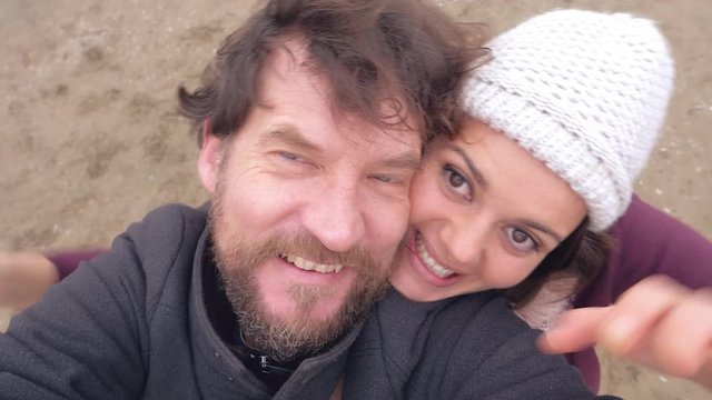 Funny couple shooting with camera playing doing selfie on beach in winter from down to high shot