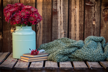 Red mums next to a pair of wire rimmed glasses sitting on antique books and next to a knubby green...