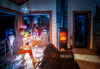 Fototapeta na wymiar Lovers in front of the fireplace. Man and woman in the cottage. Lovers rest in a country cottage. Evening room with fireplace. A family couple by the fireplace.
