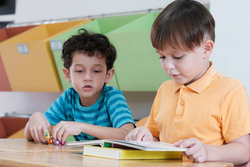 Boys reading book in their kindergarten classroom, kid education concept