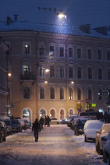 Obraz premium Silhouette of man walking along parked cars on empty evening city street during a snowstorm, selective soft focus/ heavy snowfall at St. Petersburg Russia, vertical/ Winter in St. Petersburg