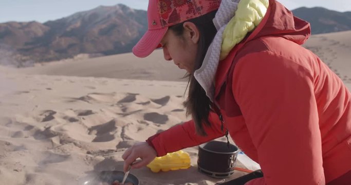 Hispanic Woman Cooking Bacon While Camping in Sand Dunes