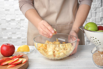 Woman putting cut apples in glass bowl on kitchen table