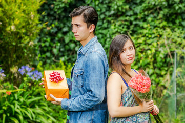 Close up of mad woman holding flowers and mad man holding a gift back to back ignoring each other, friend zone concept