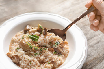 Woman eating delicious risotto with mushrooms at wooden table