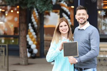 Business owner holding blank small blackboard near their store