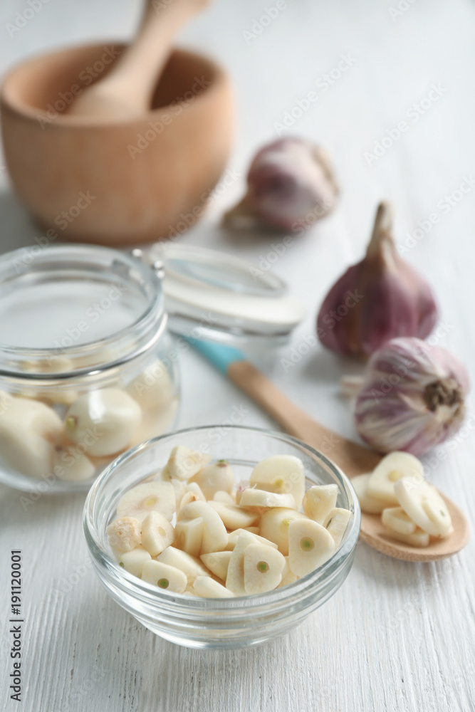 Poster bowl with chopped garlic and cloves in jar on wooden table