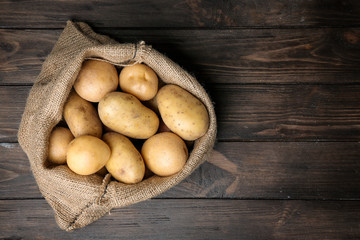 Sack of fresh raw potatoes on wooden background, top view