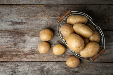 Basket with fresh raw potatoes on wooden background, top view
