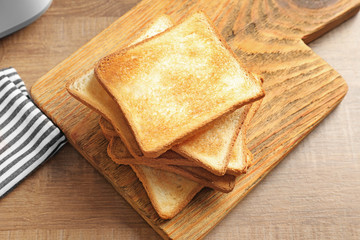 Wooden board with tasty toasted bread on table