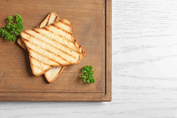 Wooden board with tasty toasted bread on table
