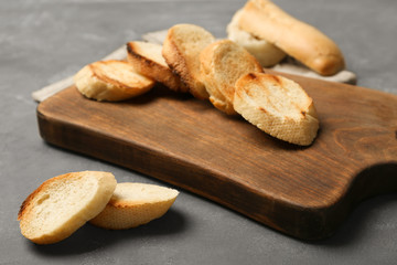 Wooden board with toasted bread on grey background