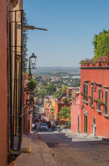 Looking down a cobblestone street, with colorful buildings and a valley way off in the distance, in San Miguel de Allende, Mexico - 191125870