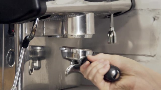 The close up of coffeemachine which is being prepared for cooking hot drinks. The equipment is made with steel and was cleaned by the barista, who is putting back the ilter for future beverage.