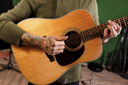 Closeup of unrecognizable tattooed man playing acoustic guitar in recording studio