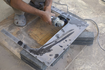 Worker cutting floor tiles with angle grinder at construction site